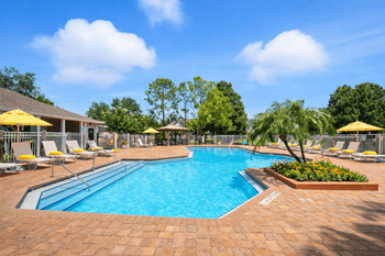 A large outdoor swimming pool surrounded by a brick patio and lounge chairs.